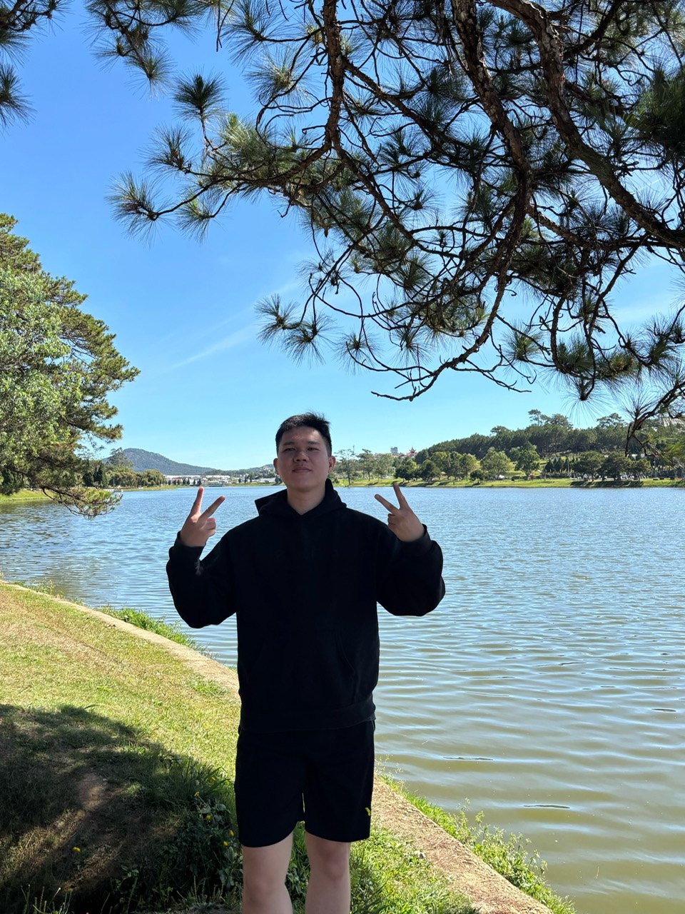 Trong Pham Tran Duc standing by a lake, pines and hills behind him